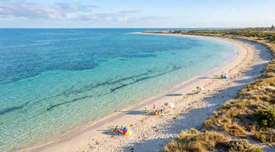 Plage aux eaux cristallines et calmes avec enfants jouant dans les vagues douces sous un ciel azur